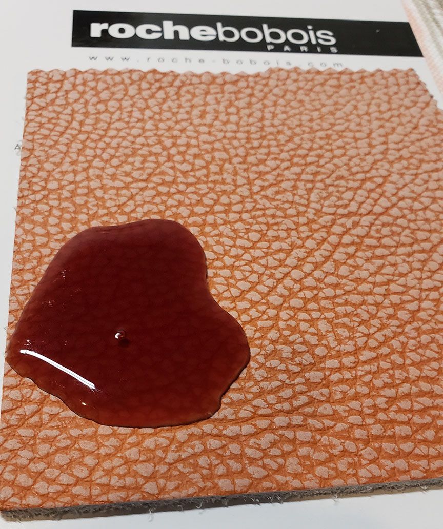 Red liquid spilled on a textured tan and orange Roche Bobois surface.