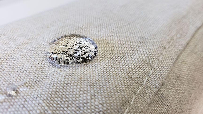 Close-up of a torn beige fabric surface with a frayed hole revealing the filling underneath