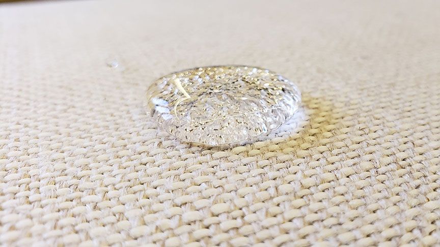 Clear water droplet on a beige woven fabric surface