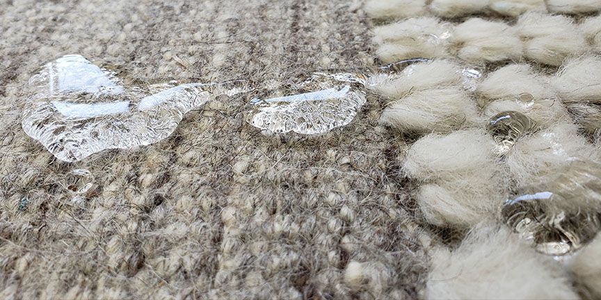 Close-up of a knitted gray-brown fabric with white fluffy yarn and a small metal ring.