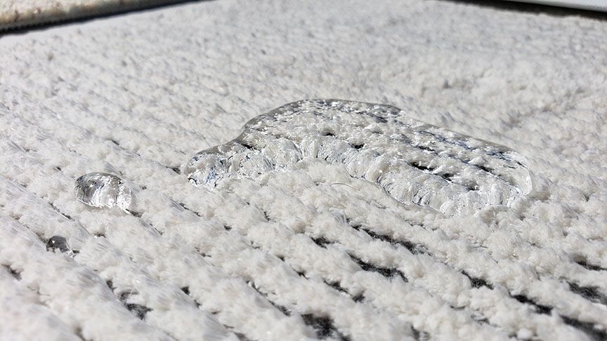 Close-up of a textured white surface with a clear droplet and dark specks