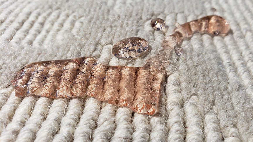 Copper-colored leaf brooch with a clear gem on a textured beige fabric background