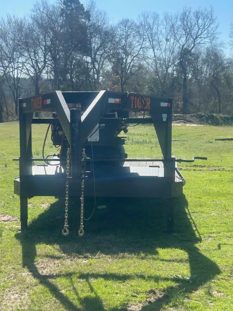 A black, heavy-duty rotary cutter mower sitting in a grassy field under a clear blue sky.