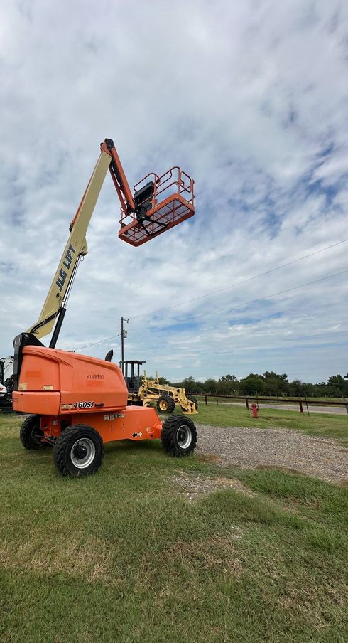 An orange boom lift with its extended platform stands on a grassy field under a cloudy sky.