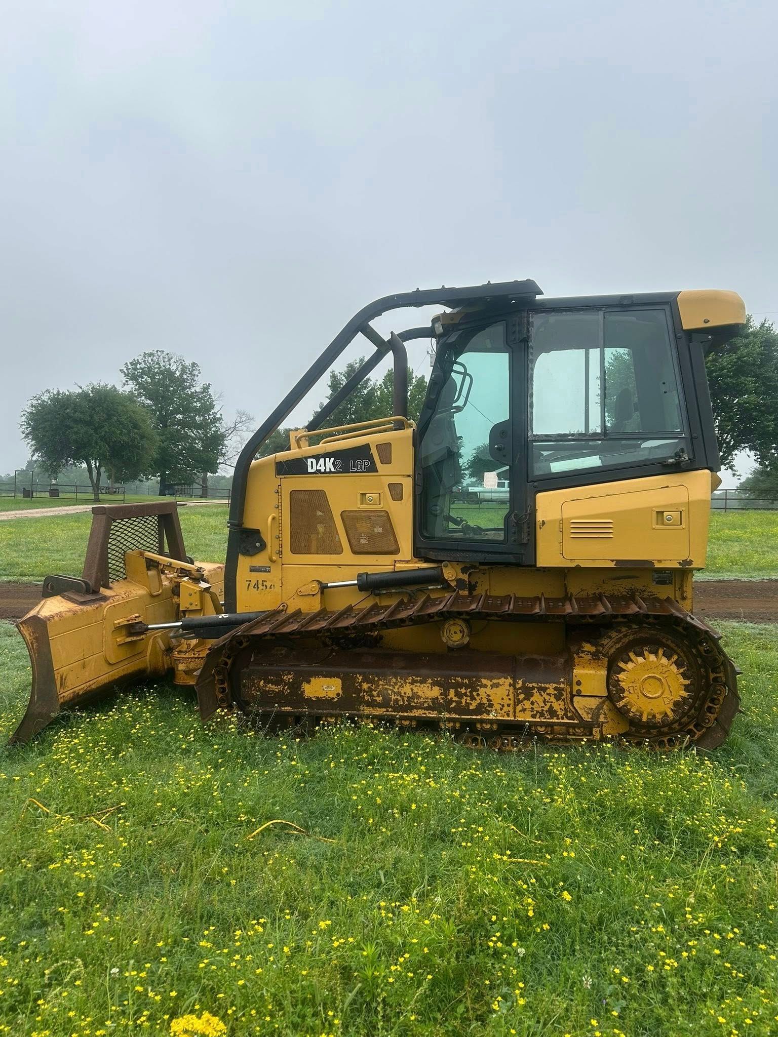 A yellow bulldozer sits on a grassy field under a cloudy, overcast sky.