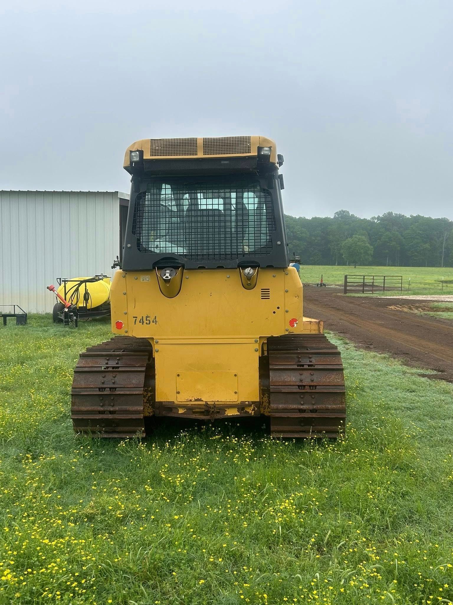 A front view of a yellow bulldozer with black tracks and an enclosed cab sitting in a grassy field on an overcast day.