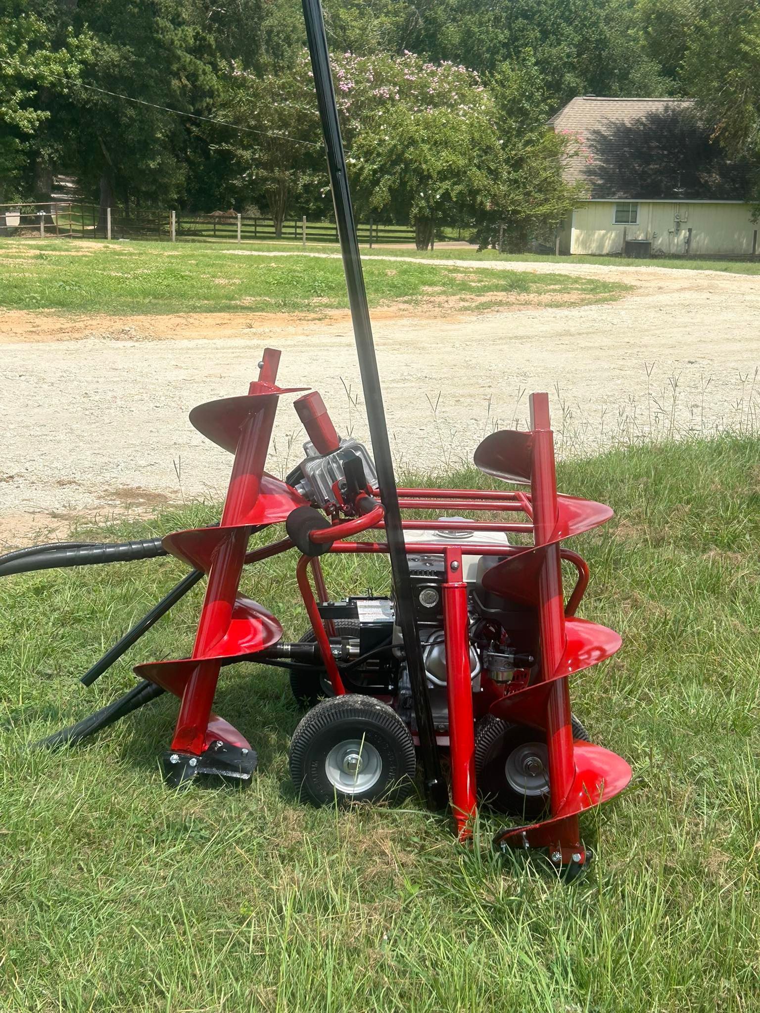 A portable, two-person red gas-powered earth auger with two drill bits attached, sitting on a grassy lawn.