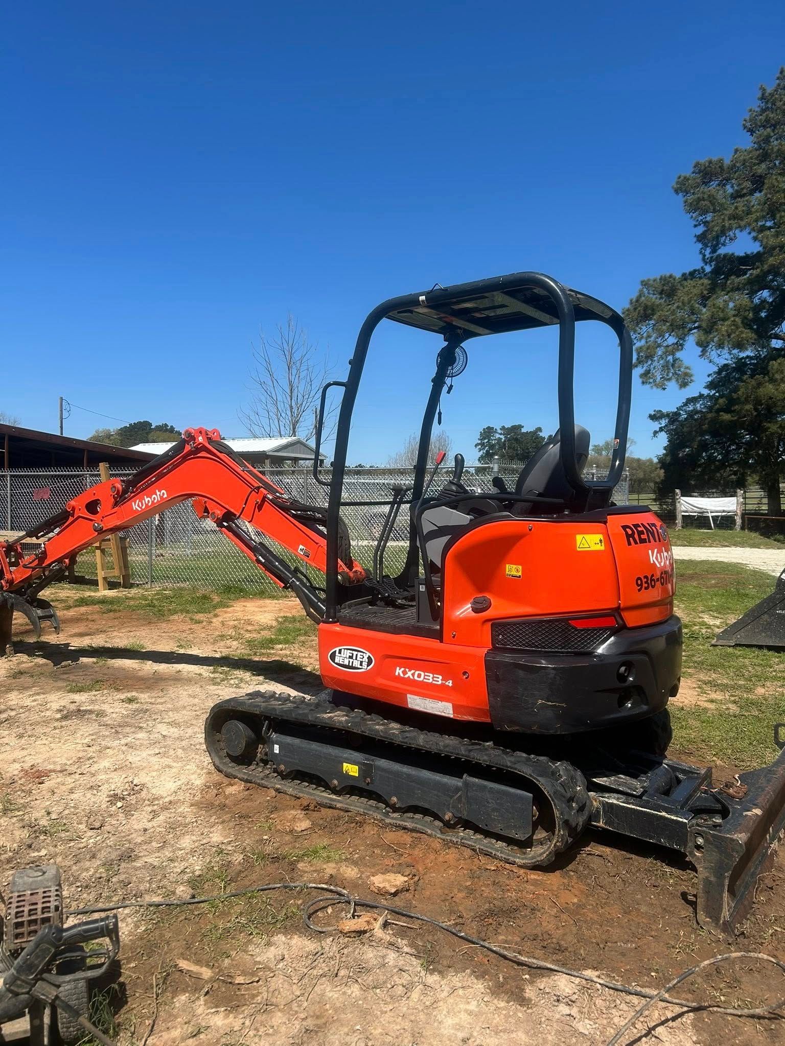 An orange Kubota compact excavator parked on a dirt lot under a bright blue sky.