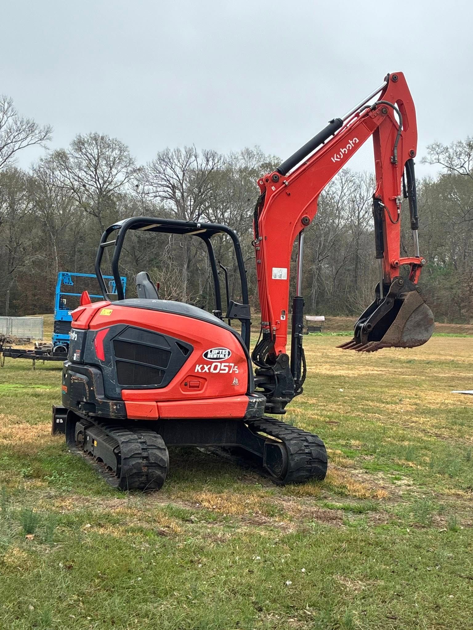 An orange and black mini-excavator parked on a grassy field with trees in the background.