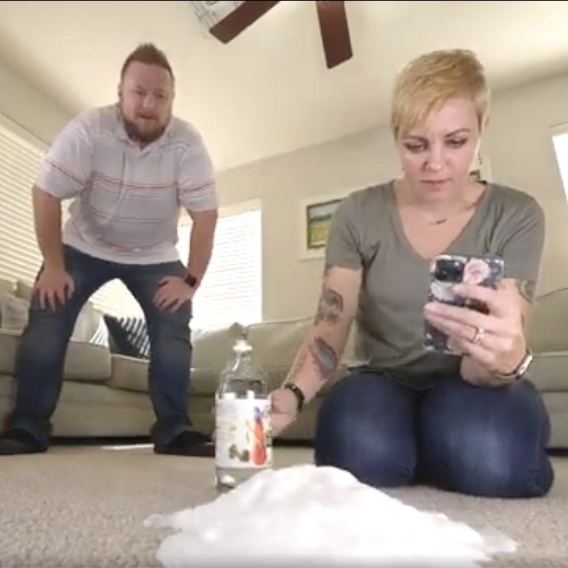A man and a woman looking at a pile of baking soda on the floor while the woman reads something on her phone