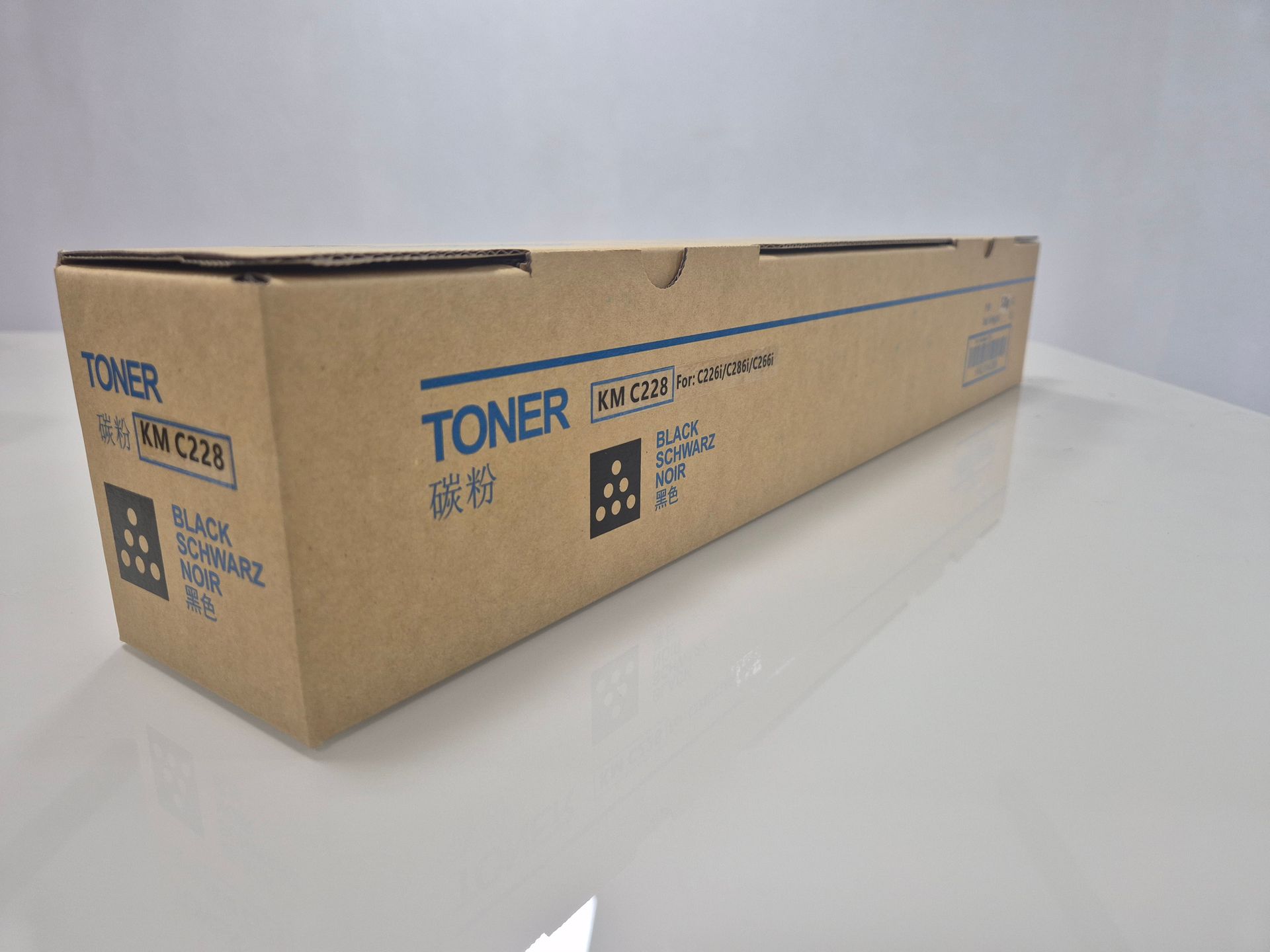 Caja de cartucho de tóner marrón con la etiqueta “TONER KM C228” y “BLACK/SCHWARZ” sobre una superficie blanca.