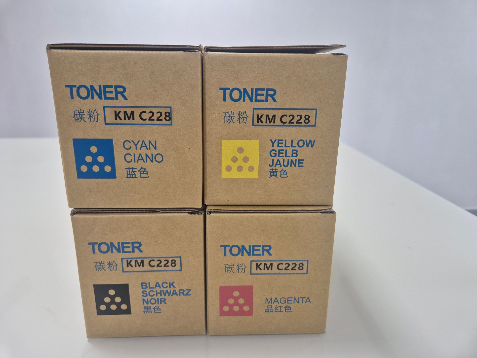 Cuatro cajas de cartón de tóner apiladas en dos filas sobre una superficie blanca contra una pared lisa.