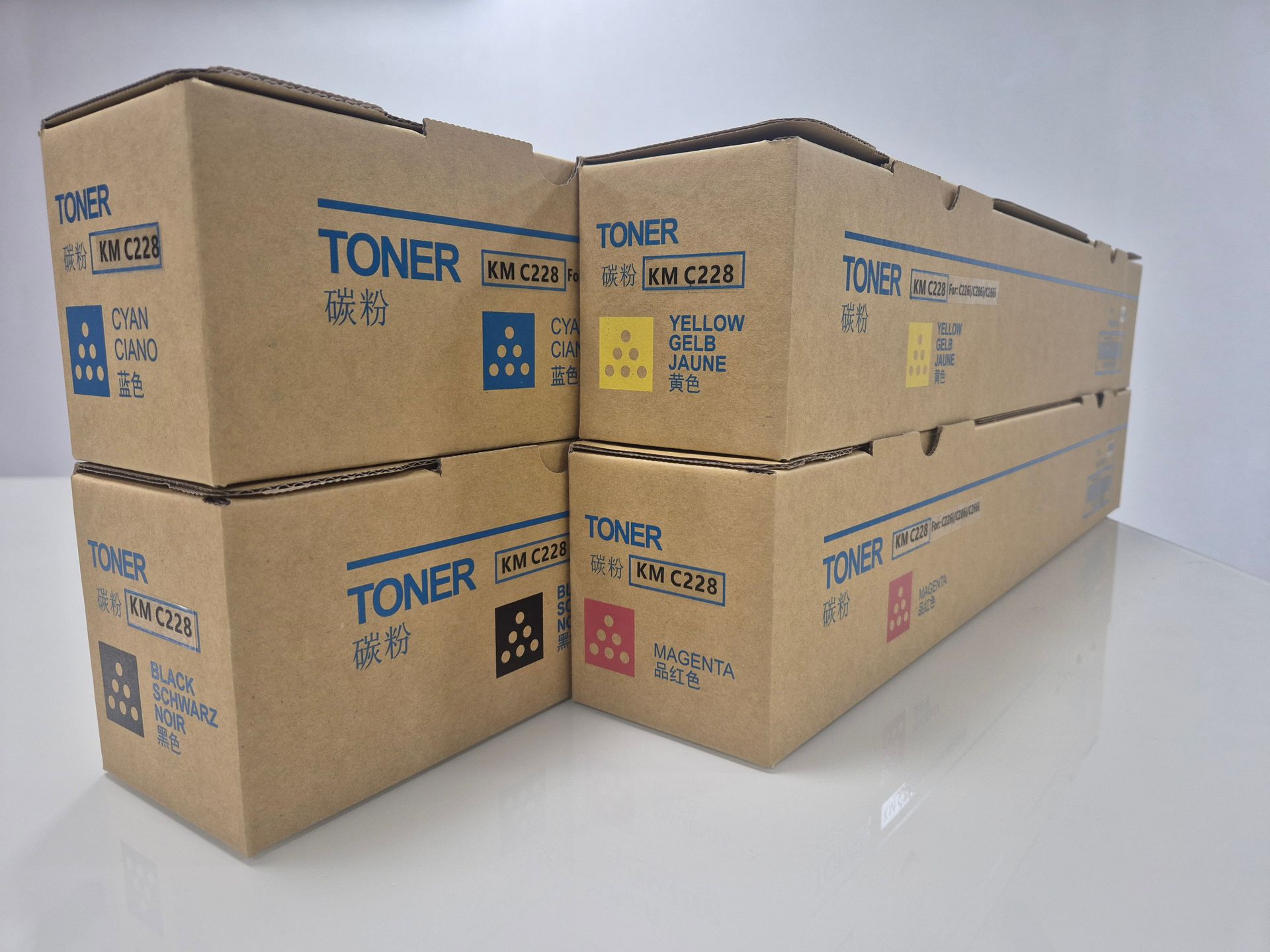 Cuatro cajas de cartón de tóner apiladas en dos filas sobre una superficie blanca contra una pared lisa.