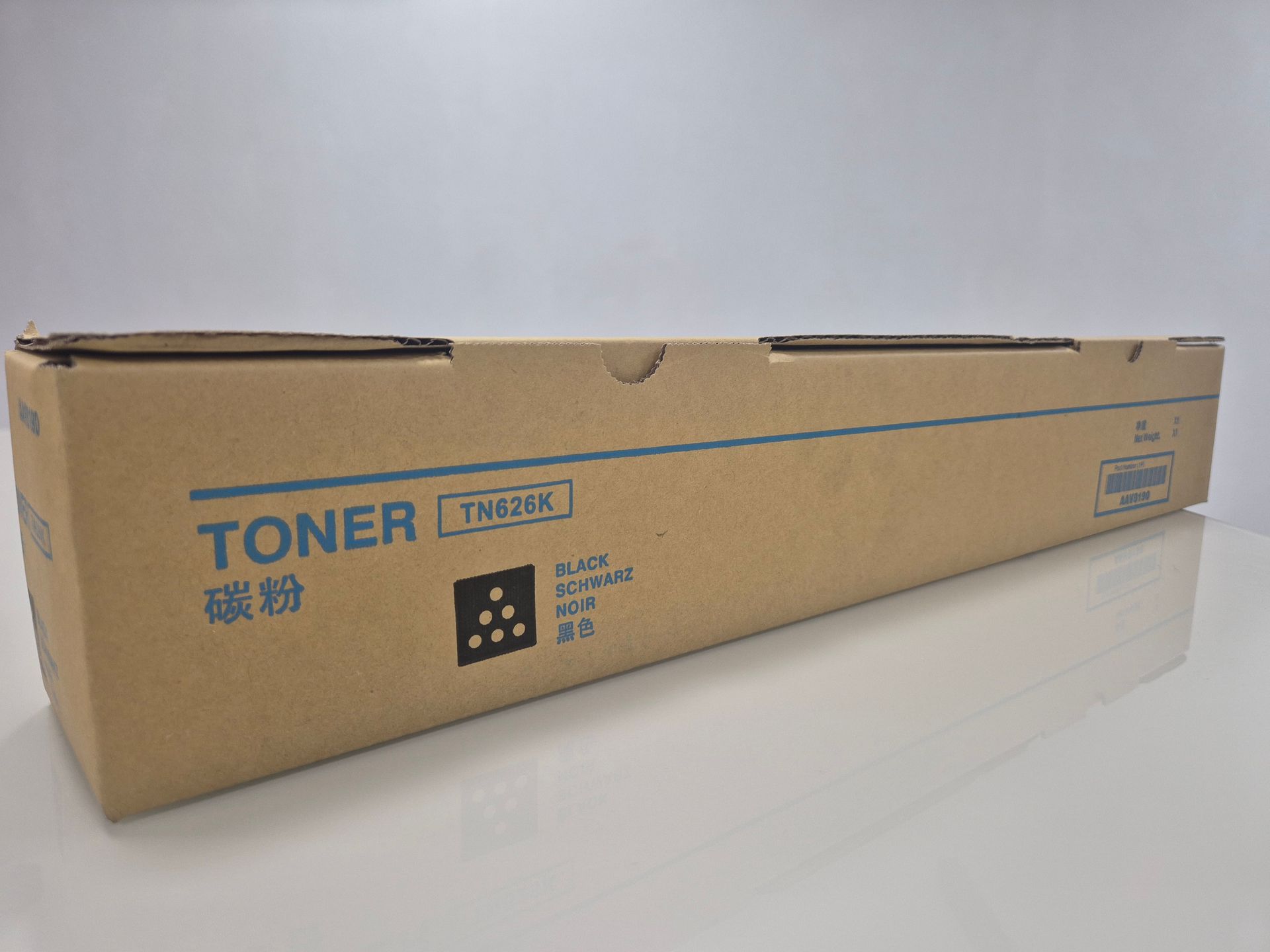 Caja de cartón alargada para tóner sobre una superficie blanca, con la etiqueta “TONER” en azul.