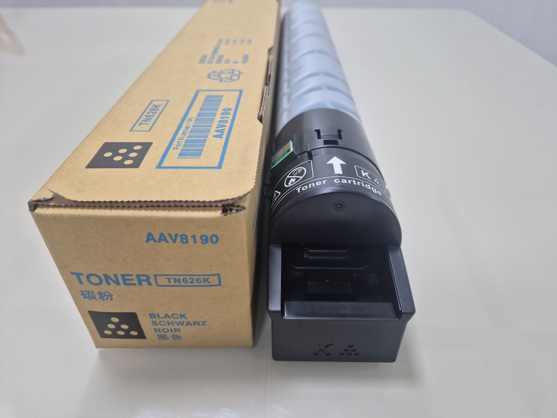 Caja de cartón alargada para tóner sobre una superficie blanca, con la etiqueta “TONER” en azul.