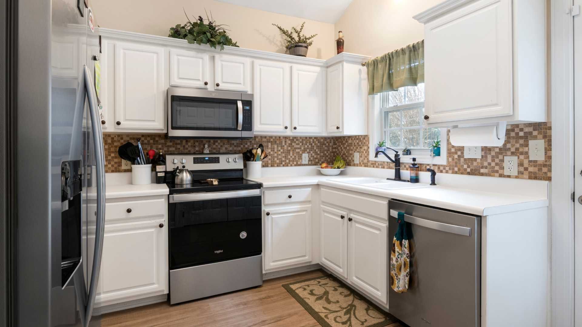 A kitchen featuring white cabinets, stainless steel appliances, a tile backsplash, and light-colored countertops.
