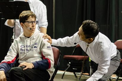A person in a white dress shirt leans forward, resting a hand on the shoulder of someone wearing a Red Bull hoodie.