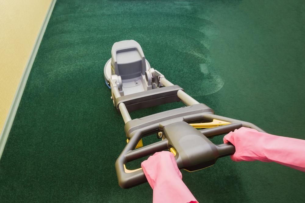 A Person Wearing Pink Gloves is Using a Machine to Clean a Green Carpet — Great Lakes Carpet Cleaning & Restoration In Pacific Palms, NSW
