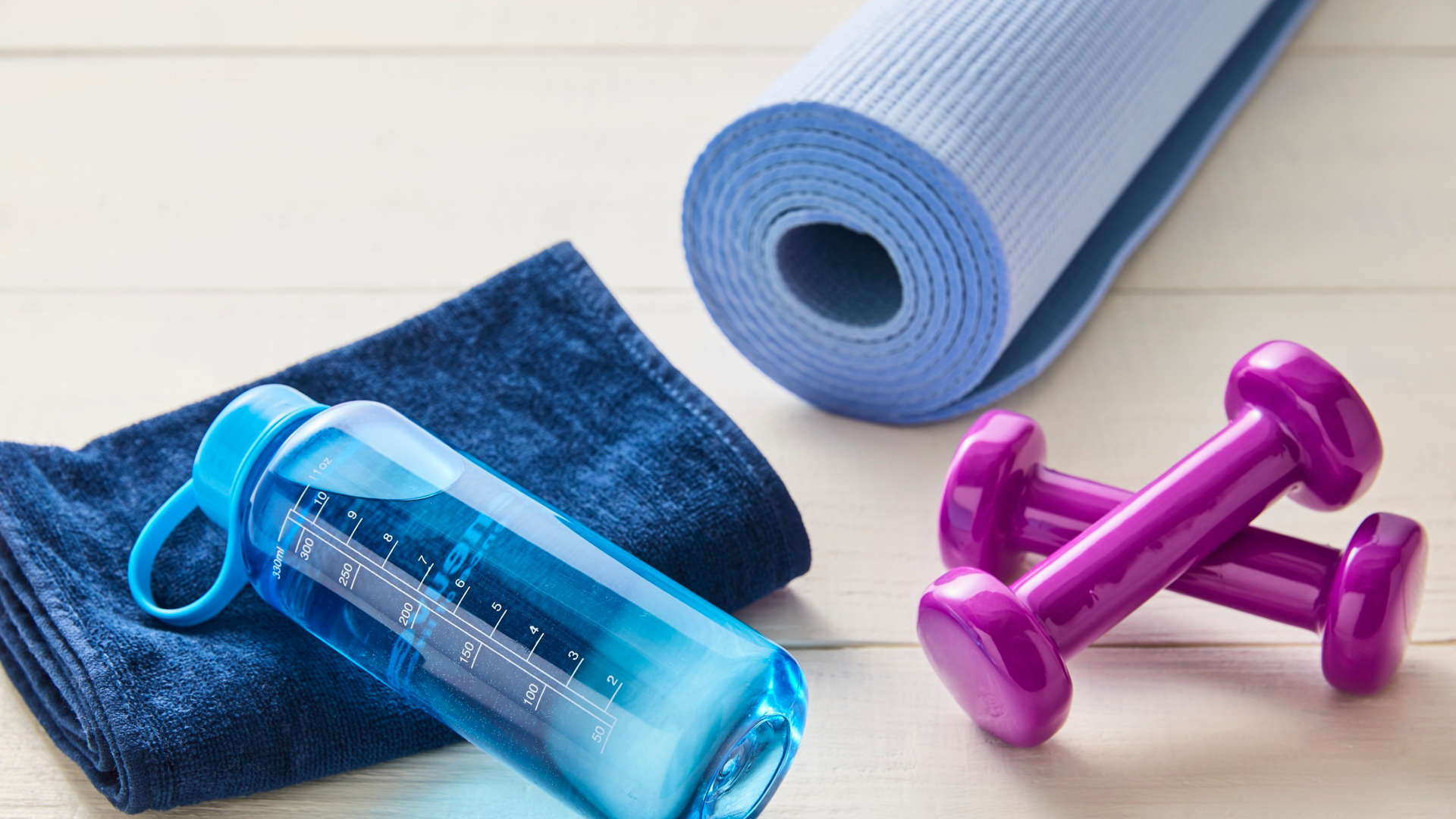 Yoga mat, pink dumbbells, water bottle, and towel arranged for a home workout