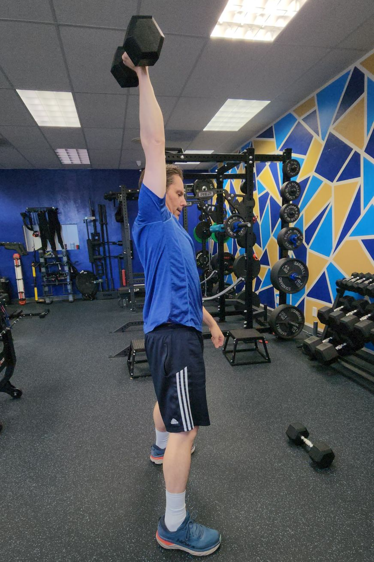 Man performing single-arm dumbbell overhead press in gym