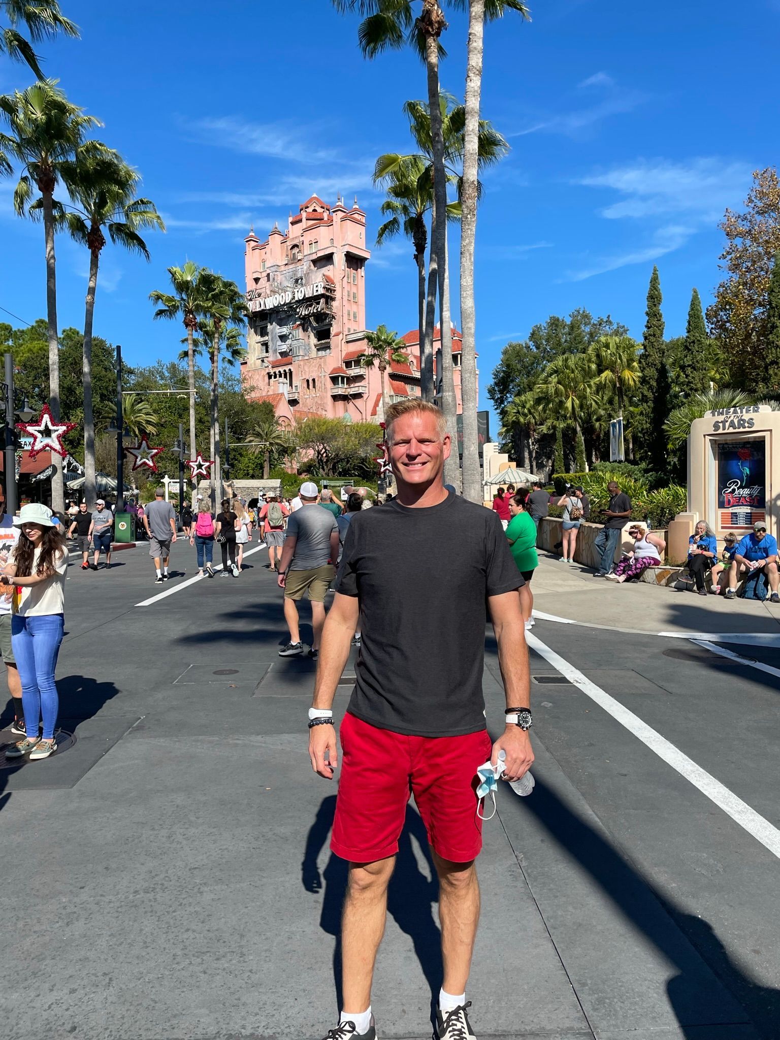 Darrell standing in a sunny theme park walkway, wearing a black shirt and red shorts