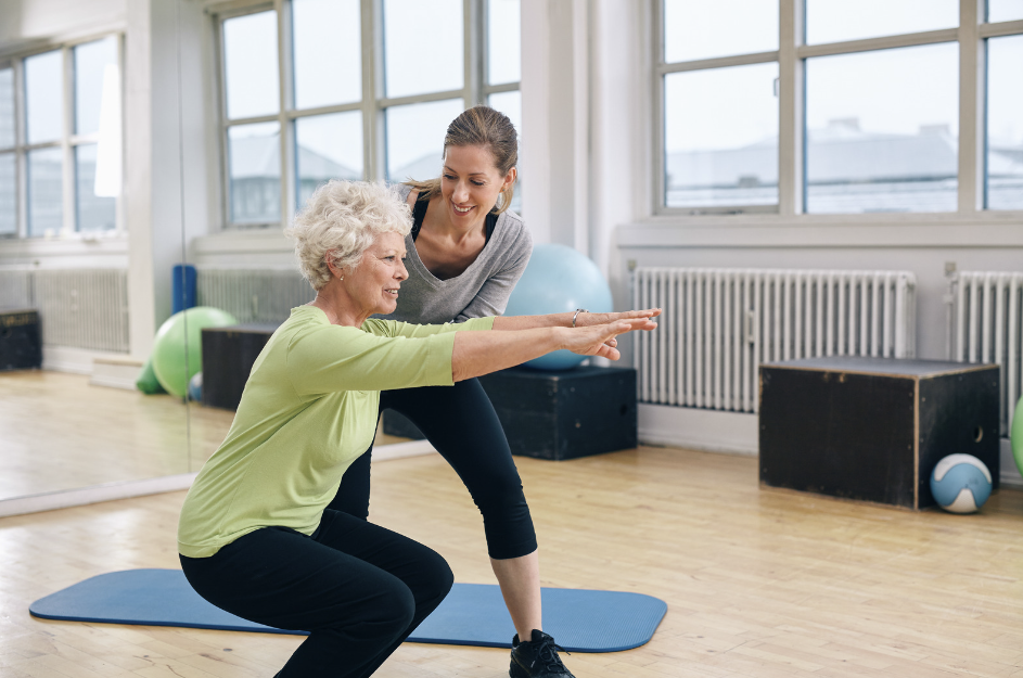Trainer supports senior woman performing a squat