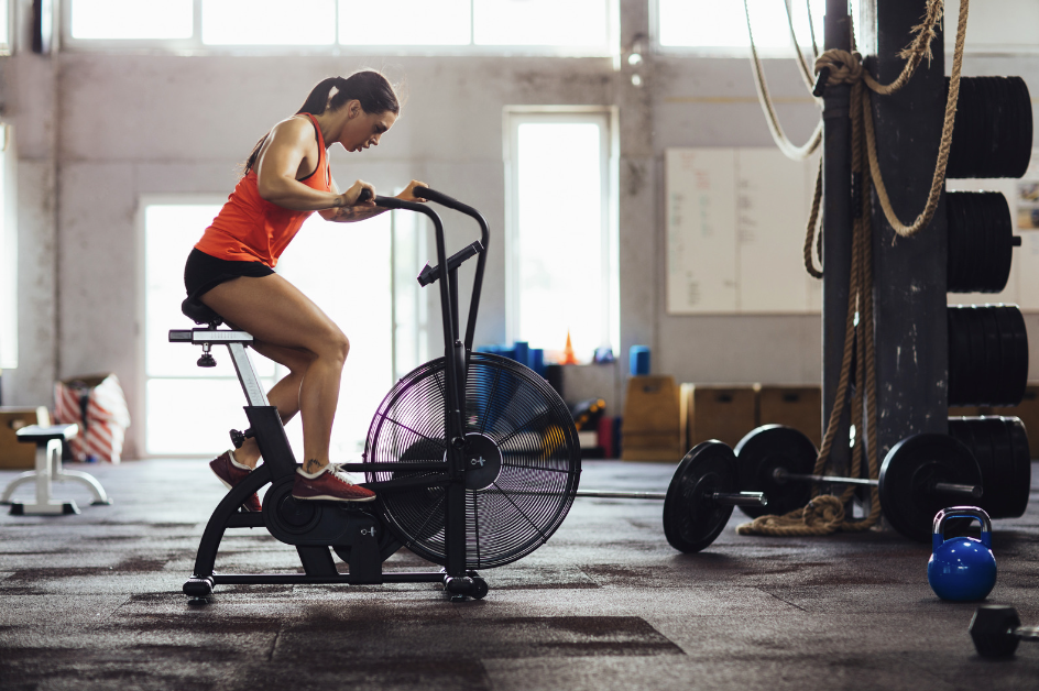 Woman performing high intensity cardio workout on air bike in gym