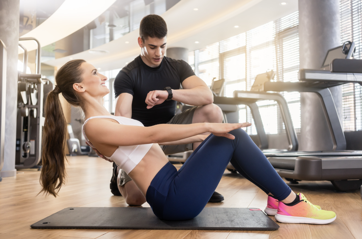 Personal trainer guiding woman performing core exercise on mat in gym