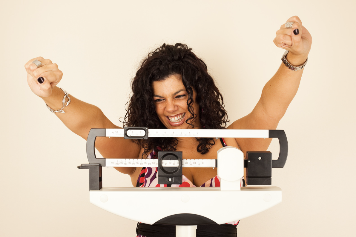 Woman smiling on scale during weight loss journey