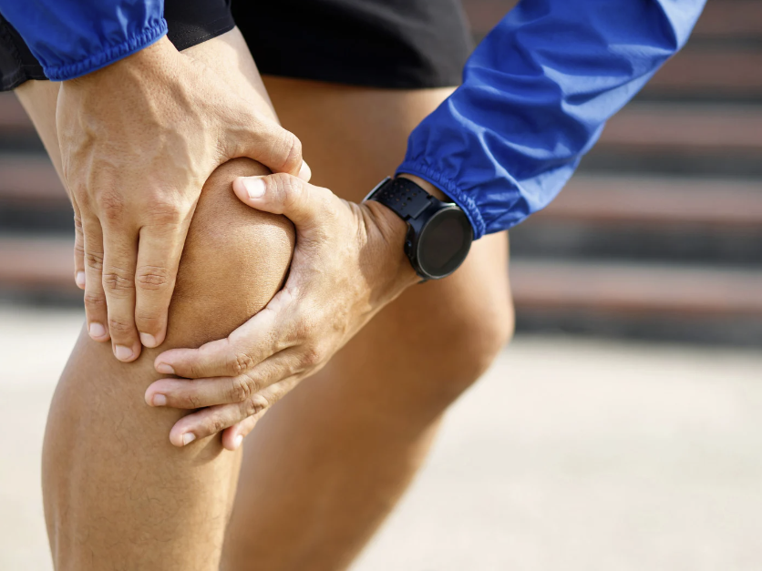 Close-up of a person clutching their knee in pain while wearing a fitness tracker,