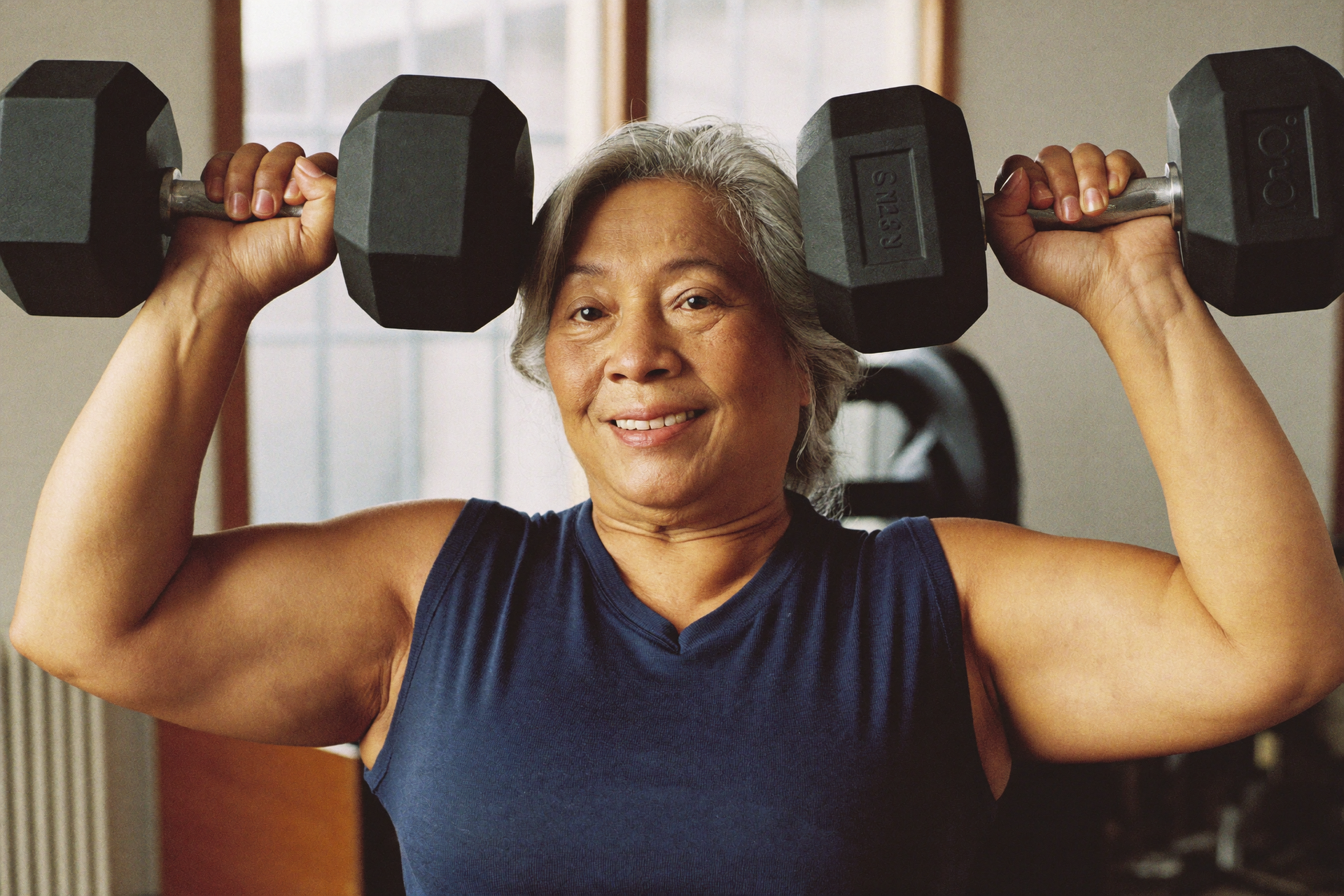 A woman in her fifties presses dumbbells overhead with controlled form.