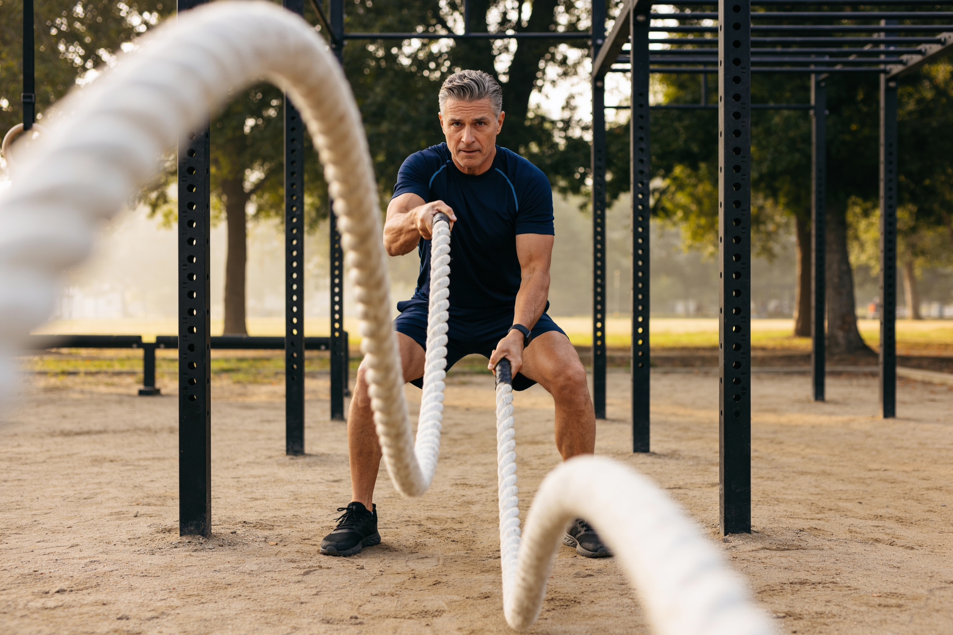 An adult trains with battle ropes at an outdoor gym, putting consistent structured effort into a core movement.