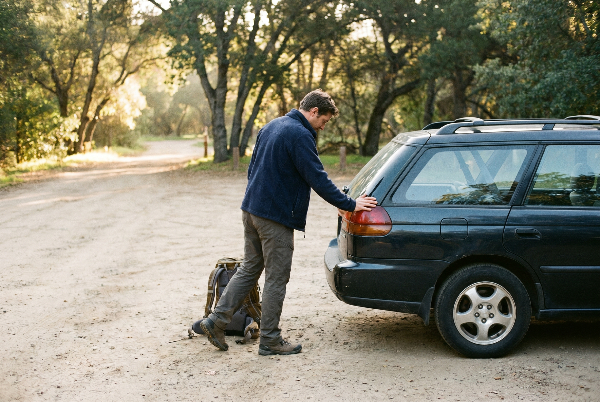 Hiker doing a calf and ankle warm-up beside the car at a trailhead.