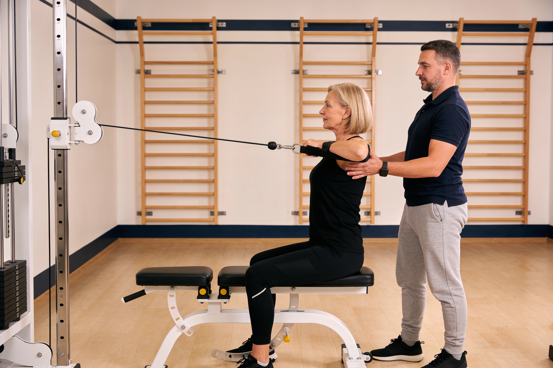 Coach guiding a woman through a supported band row with attention to grip and control.