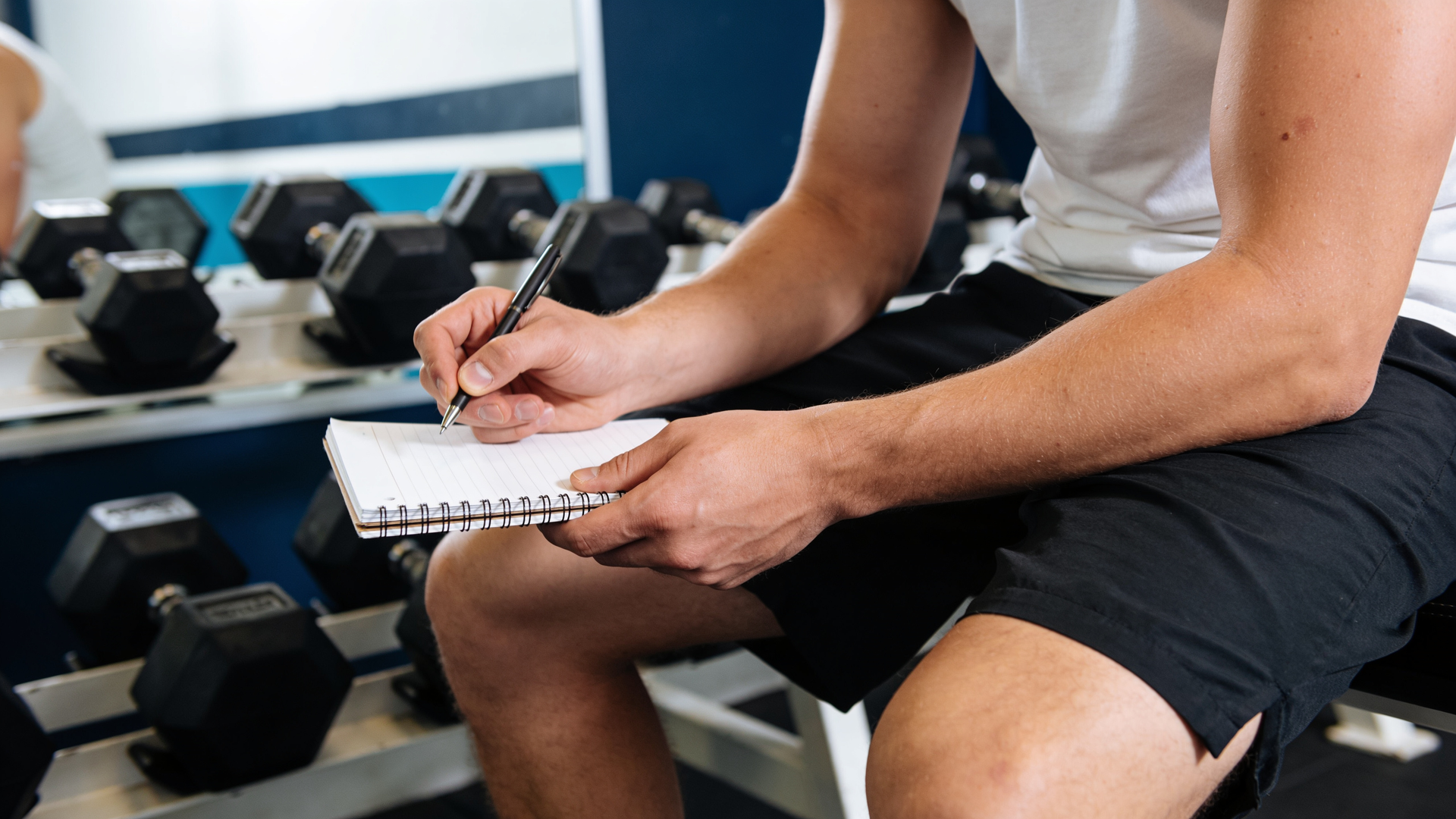 An adult pausing between sets to note weights and reps in a training log.
