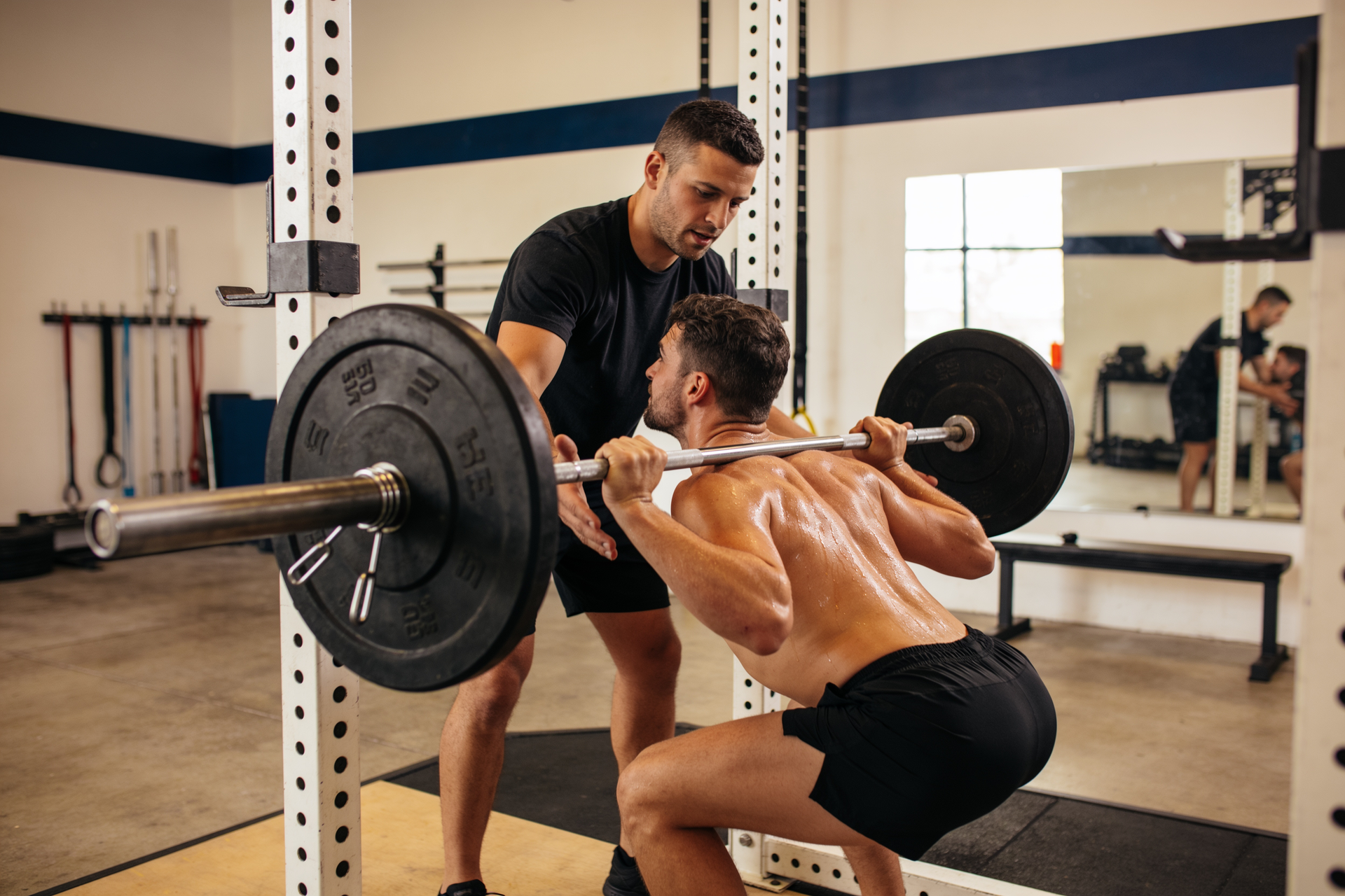 A coach spotting a client through a hard barbell back-squat set near a real limit.