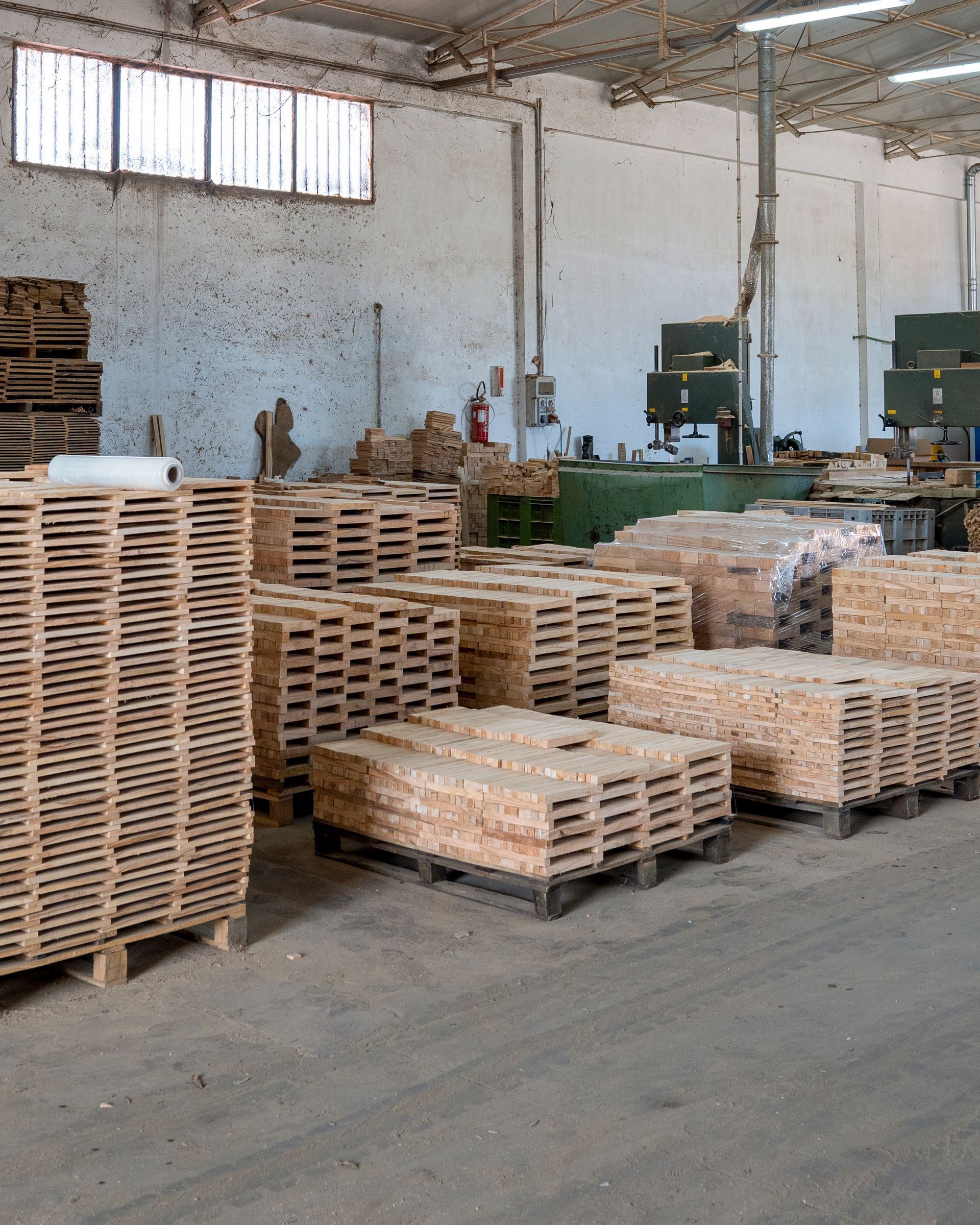 Pile di pallet di legno in un magazzino con macchinari industriali e muri di mattoni.