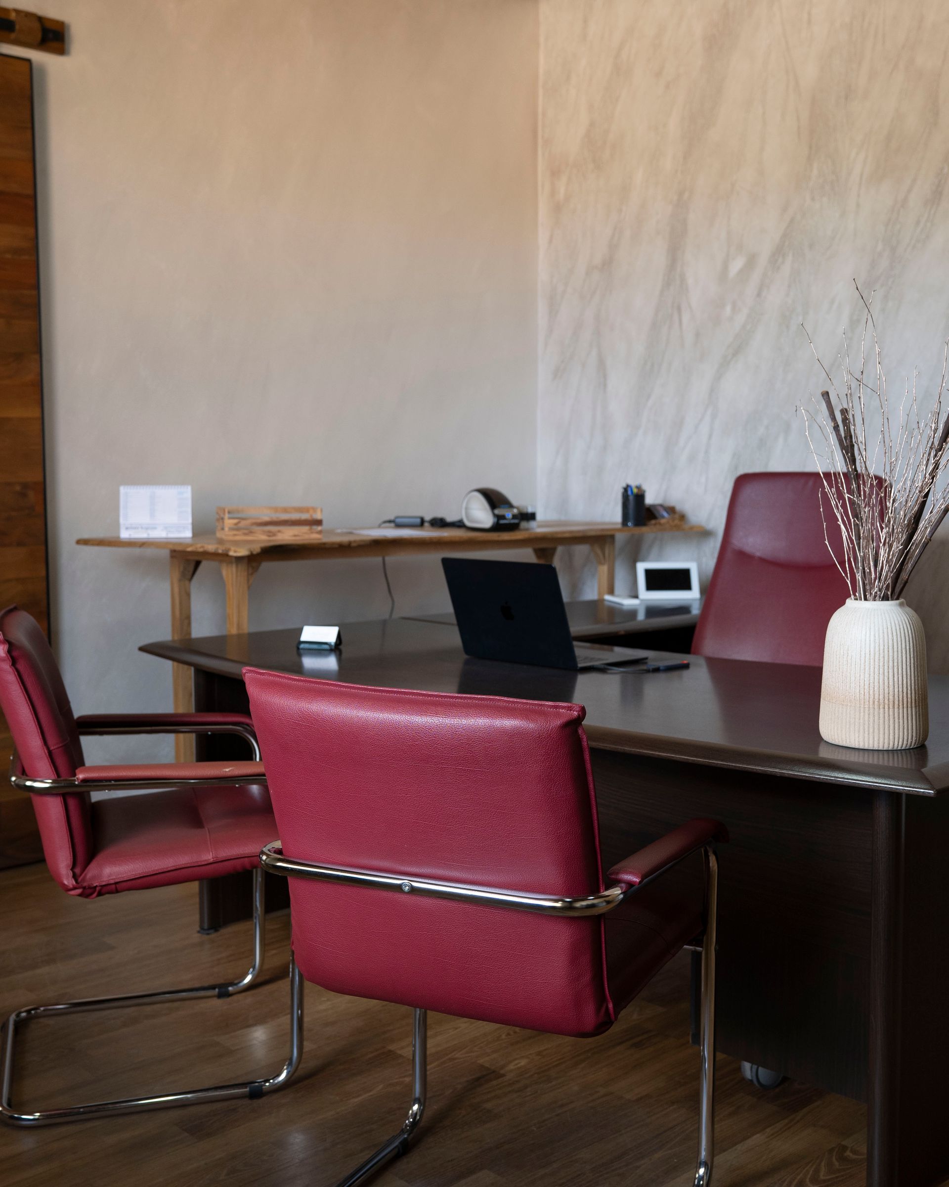 Sala conferenze in ufficio con sedie color bordeaux, tavolo scuro e un vaso con rami.