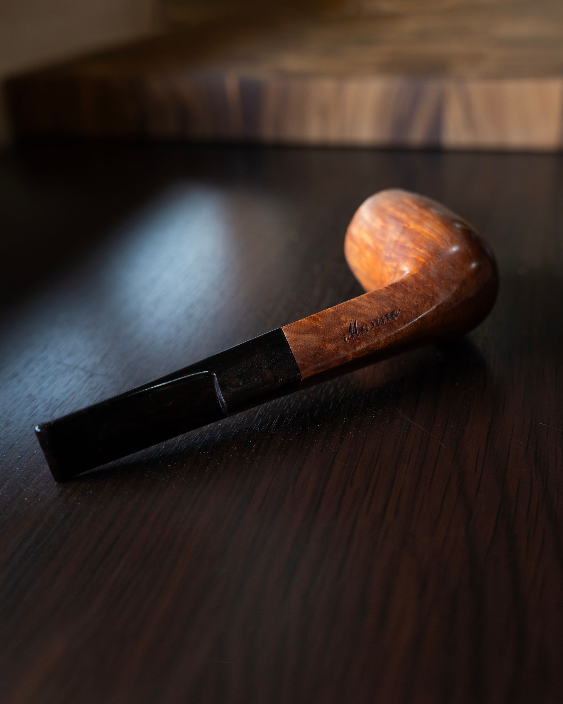 Una pipa di legno su un tavolo scuro, illuminata da una luce soffusa.