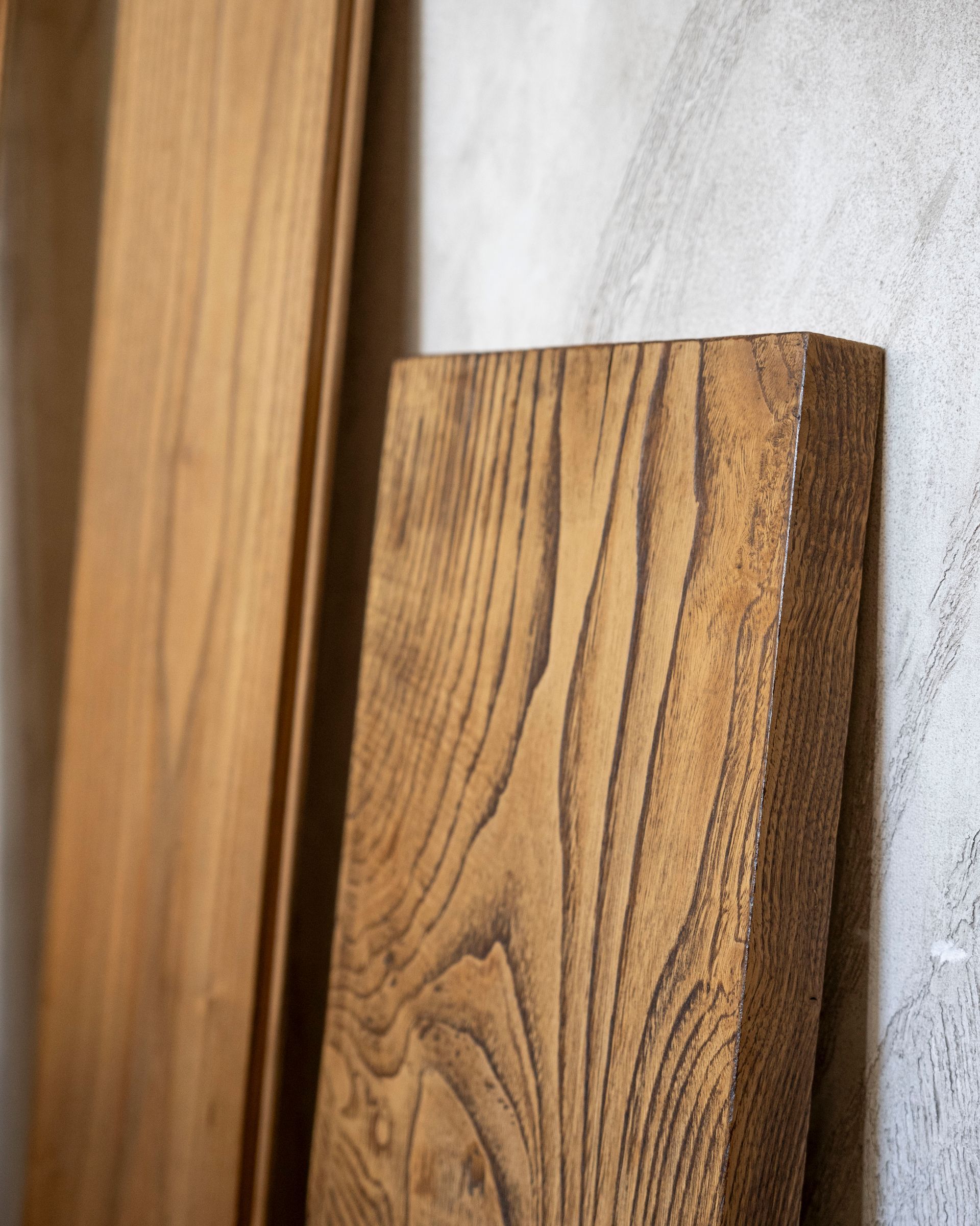 Primo piano di assi di legno con venature ben visibili, appoggiate a una parete grigio chiaro.