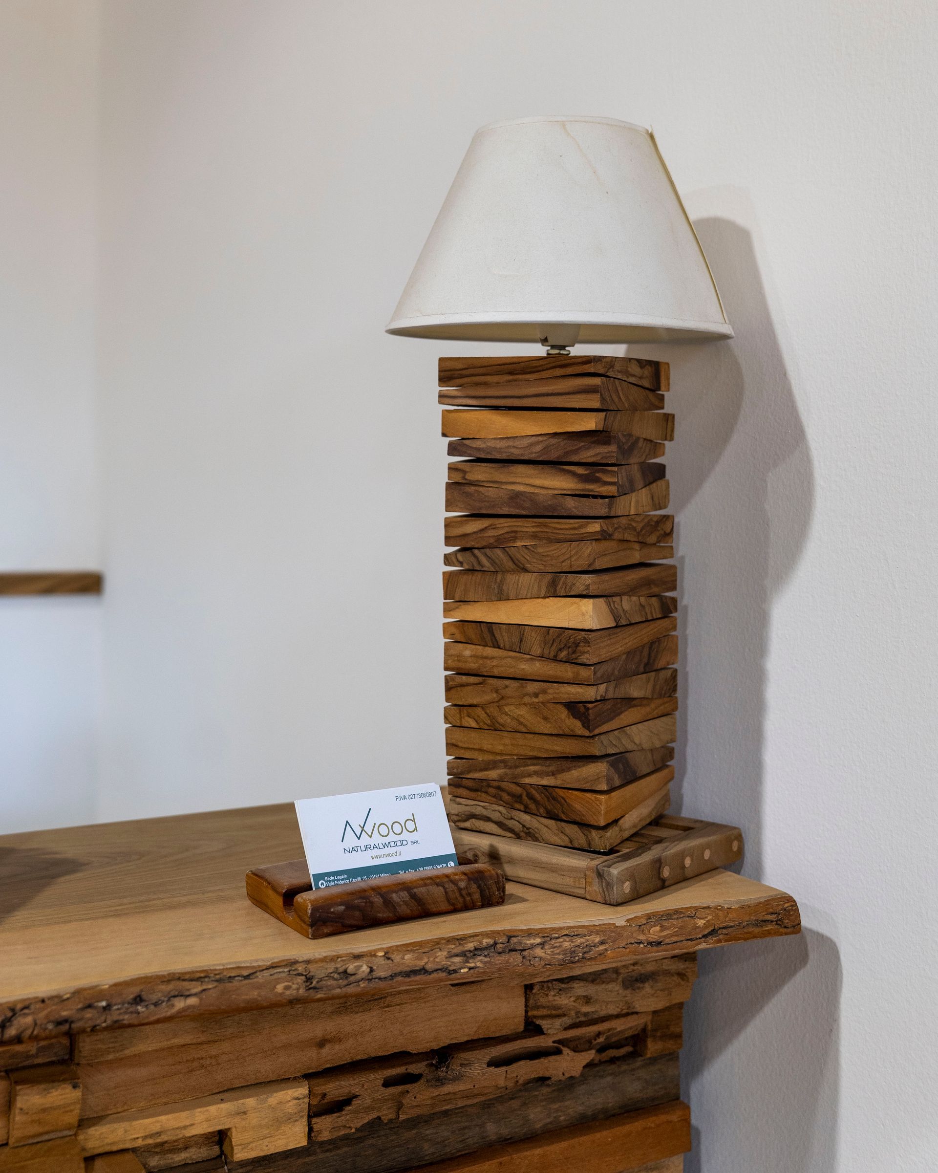 Lampada da tavolo rustica in legno impilato con paralume bianco su una superficie in legno