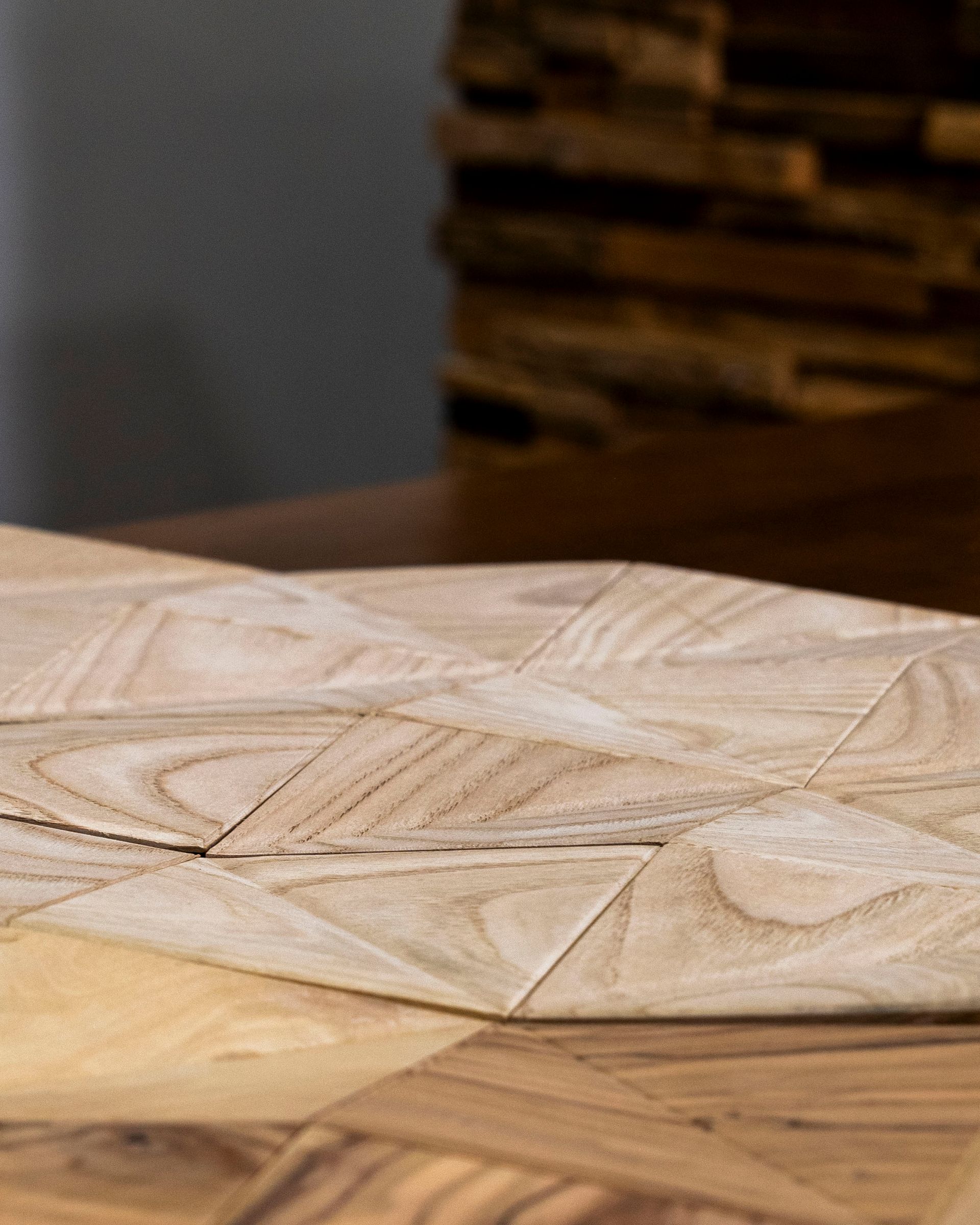 Primo piano di un tavolo in legno intagliato con motivi geometrici e una catasta di legna sfocata sullo sfondo.
