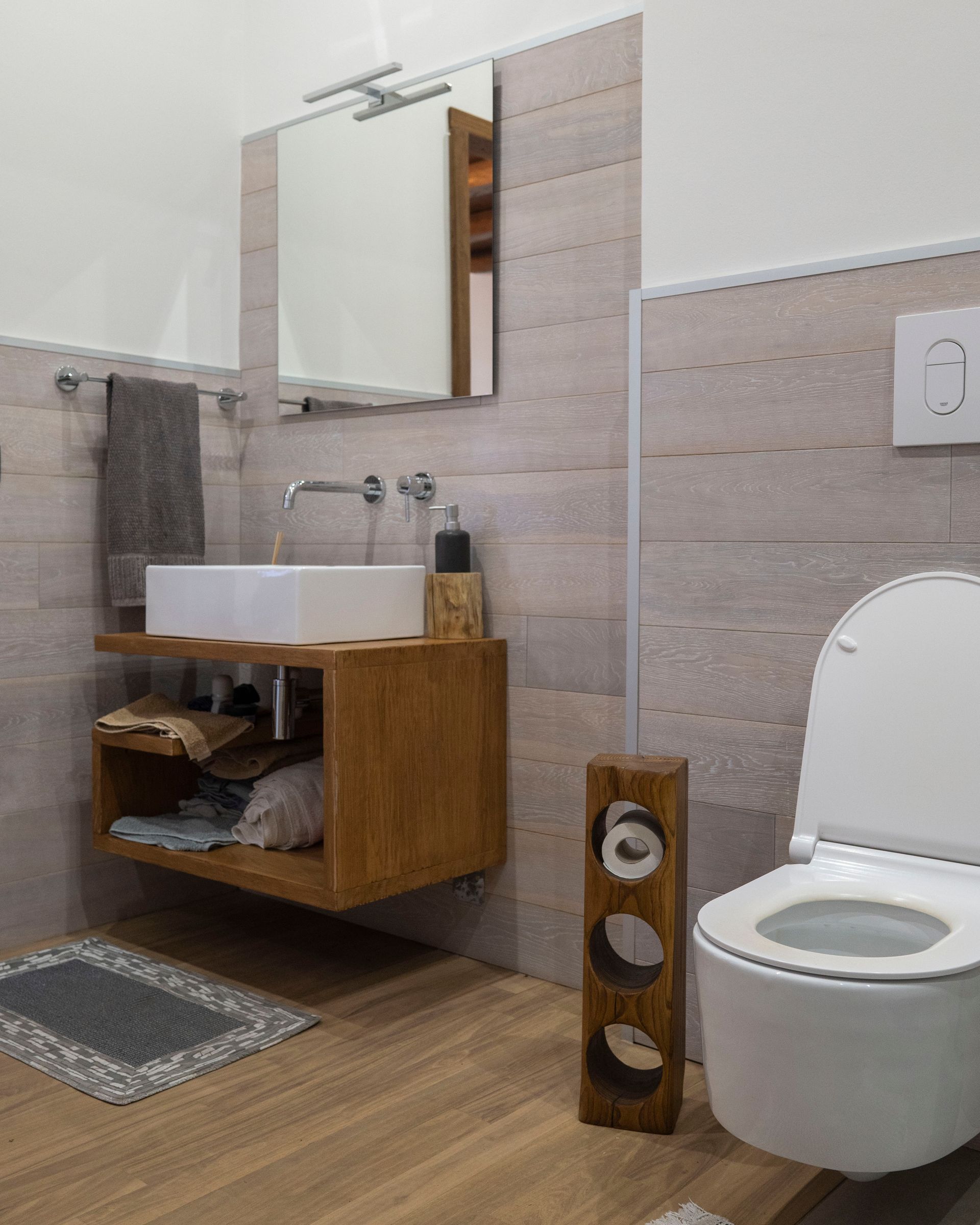 Bagno moderno con mobiletto in legno, lavabo a ciotola, specchio, WC e pareti piastrellate.