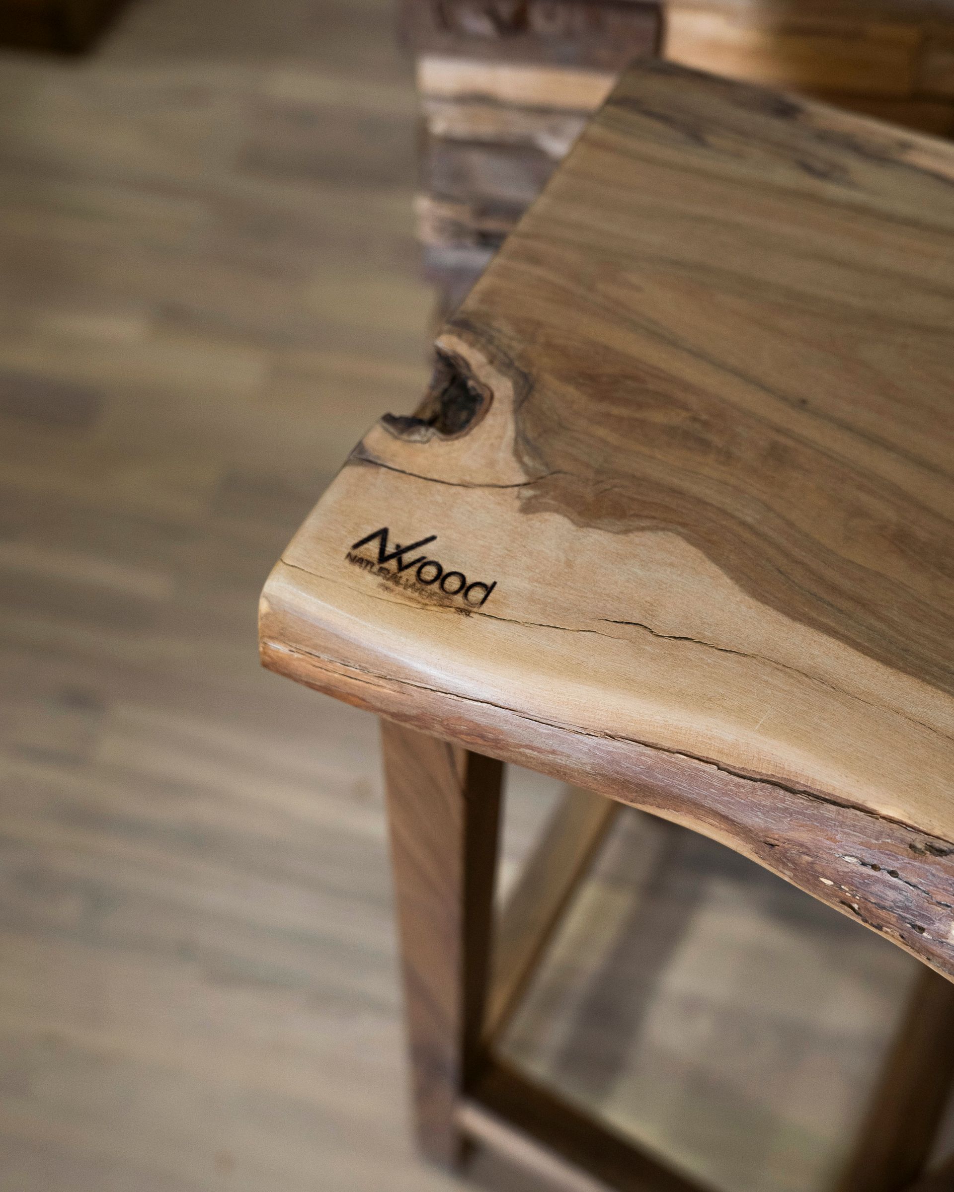 Primo piano di uno sgabello in legno con piano a bordo naturale e venature del legno ben visibili.