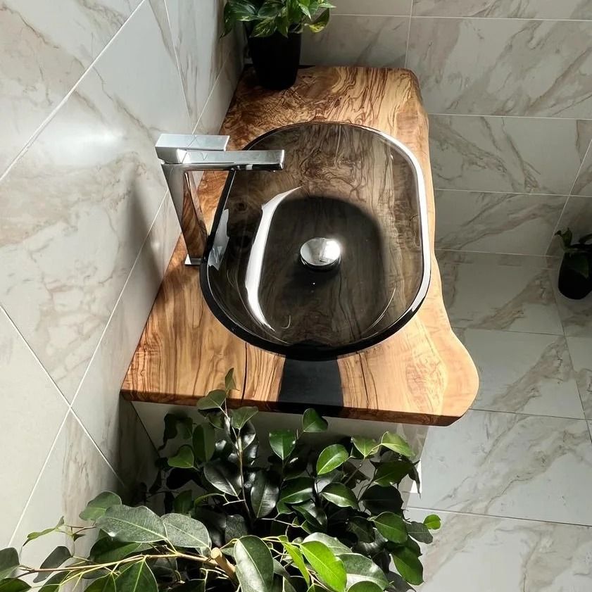 Lavabo in vetro nero su un piano di lavoro in legno con rubinetto cromato, circondato da piante verdi.