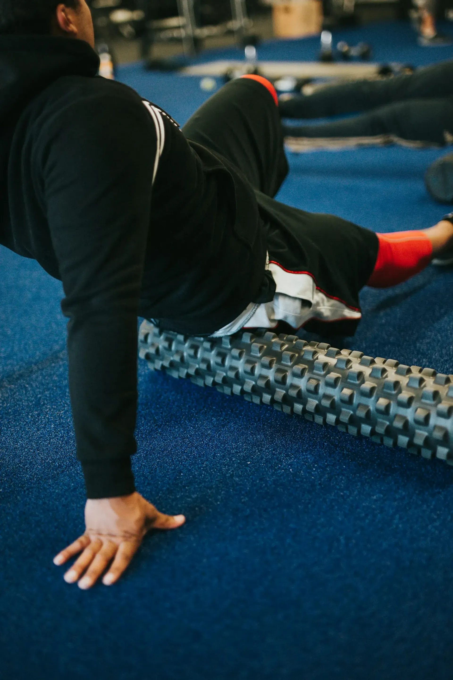 A man is stretching his leg on a foam roller in a gym.