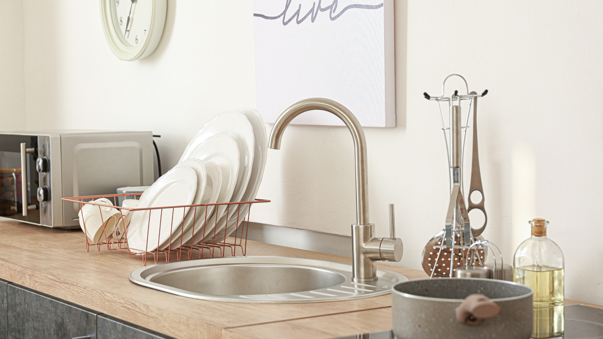 A kitchen with a sink , a microwave , and a clock on the wall.