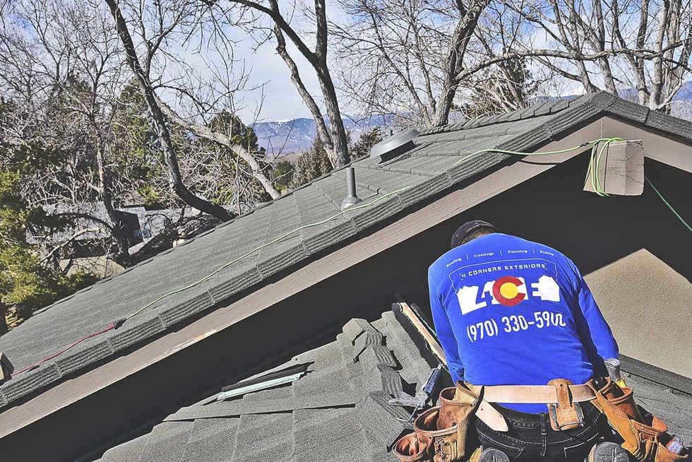 Person wearing a blue Colorado helmet near a house roof with trees and mountains in the background