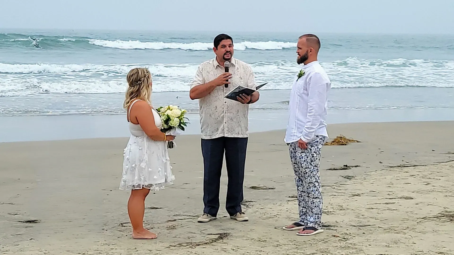 Wedding ceremony on a beach: Bride, groom, officiant stand before ocean waves.