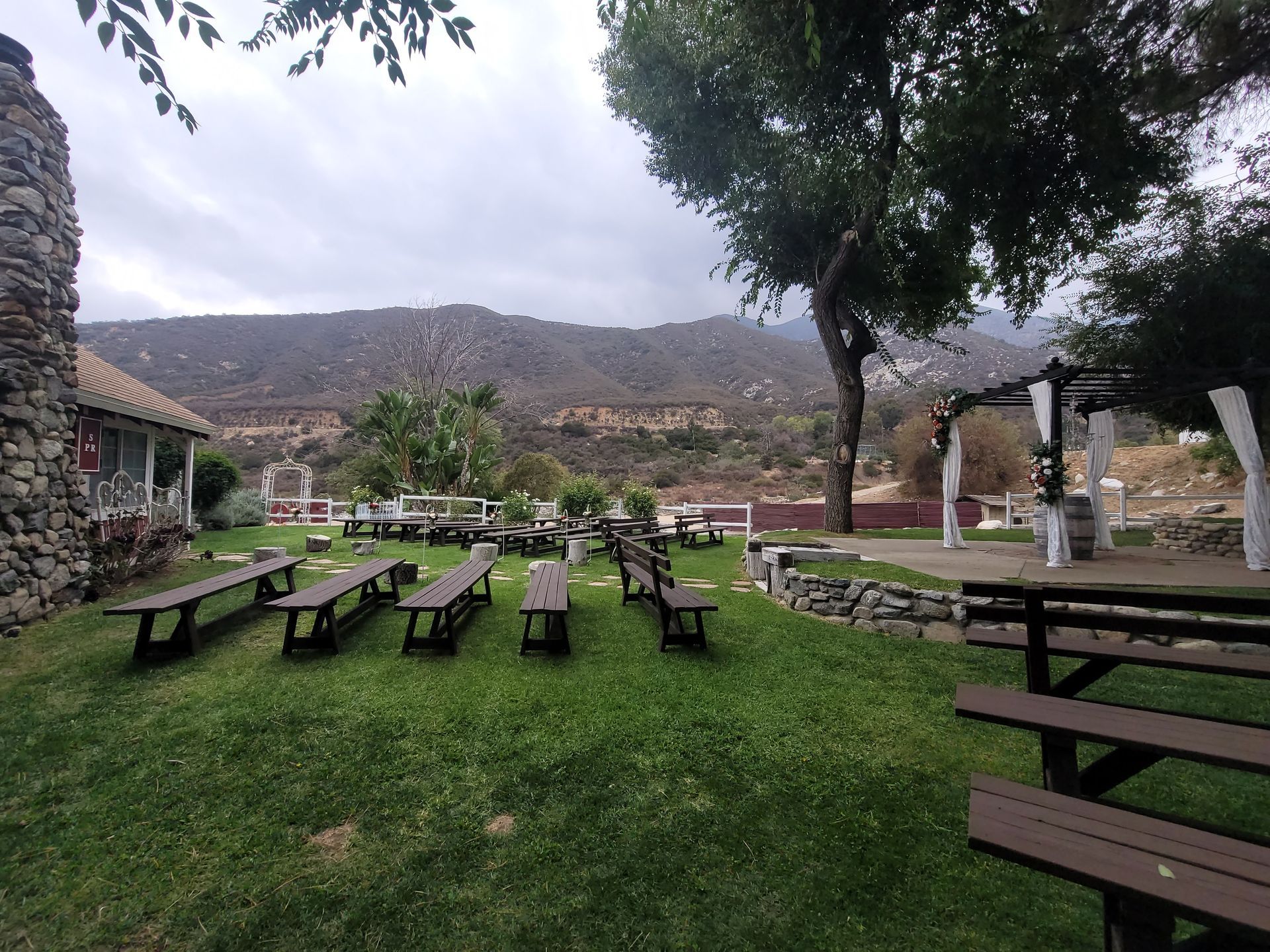 Outdoor wedding venue with benches on grass, mountain backdrop, overcast sky.